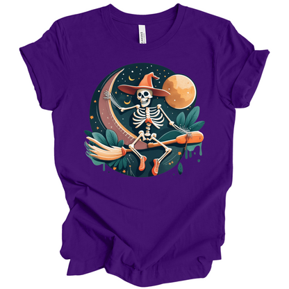 Purple halloween t-shirt with a skeleton on a broomstick wearing a witch hat in the night time.